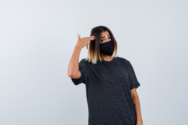 Free photo lady making suicide gesture in black dress, medical mask and looking depressed. front view.