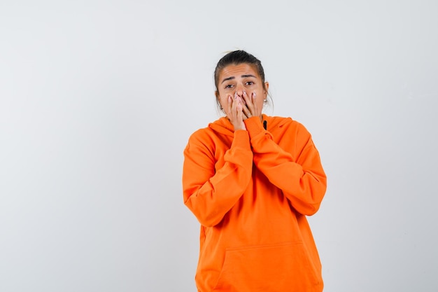 Lady in orange hoodie keeping hands on mouth and looking excited