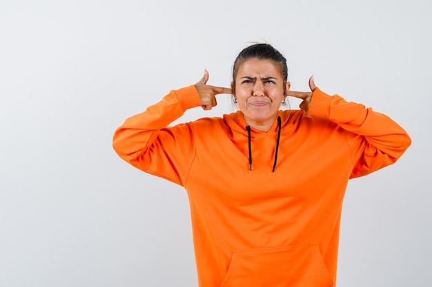 Lady in orange hoodie plugging ears with fingers and looking irritated