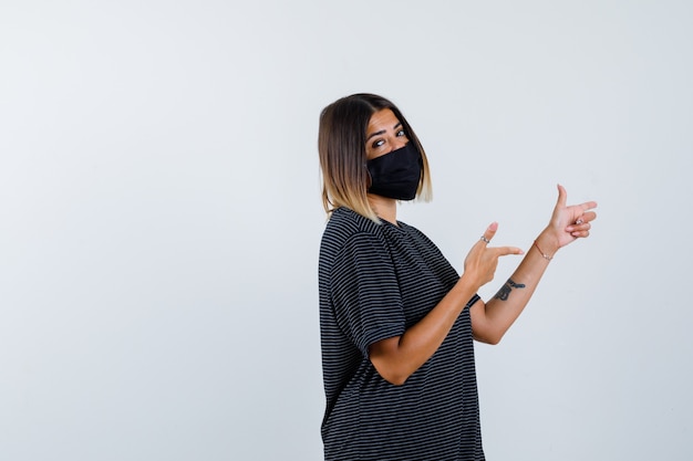 Free Photo lady pointing right in black dress, medical mask and looking confident. front view.