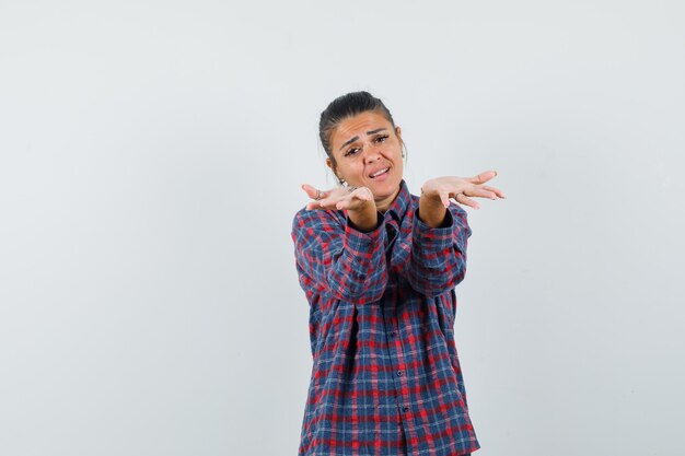 Lady raising open palms in casual shirt and looking helpless , front view.