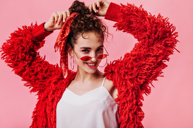 Lady in red outfit and sunglasses smiling on pink background