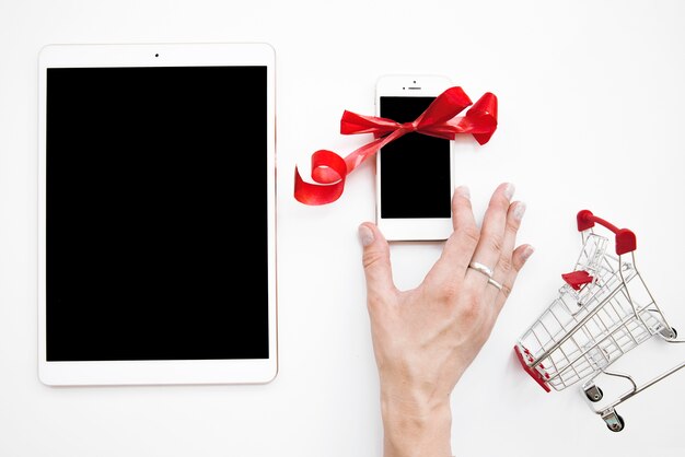 Lady's hand on smartphone near tablet and shopping trolley