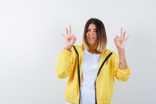 Lady showing ok gesture in t-shirt, jacket and looking happy. front view.