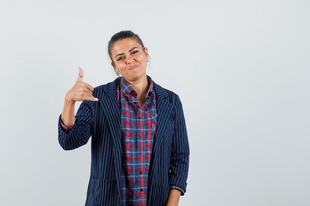 Lady showing phone gesture in shirt, jacket and looking confident. front view.