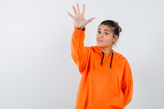 Lady showing stop gesture in orange hoodie and looking confident