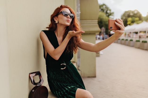 Free photo lady in sunglasses blows kiss while taking selfie