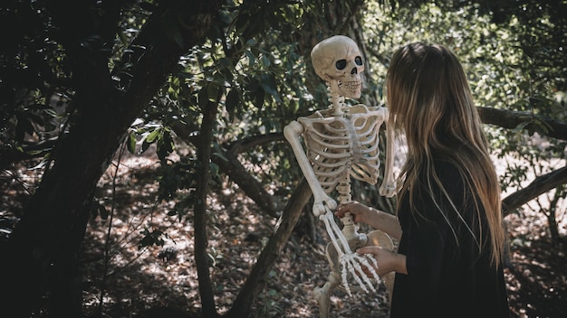 Free photo lady in witch costume keeping skeleton