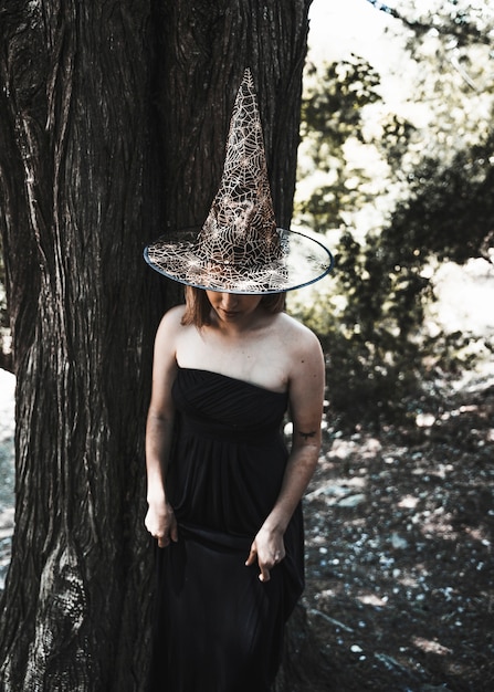 Free photo lady in witch costume standing near tree