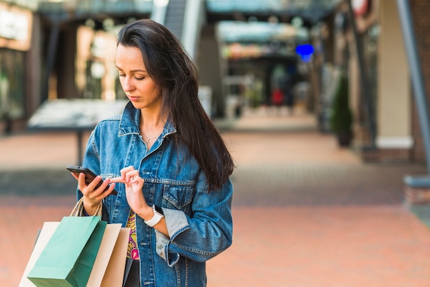 Free photo lady with shopping bags using smartphone in mall