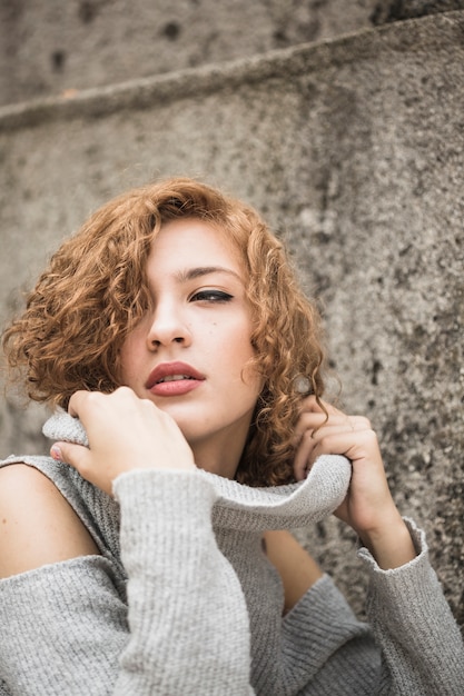 Lady with short curly hair holding sweater's collar 