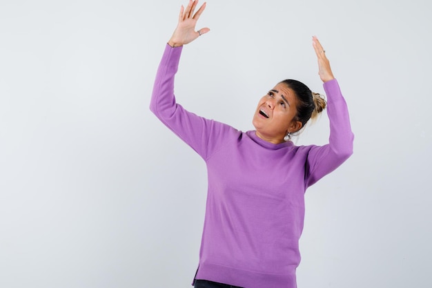 Lady in wool blouse raising hands while looking up and looking surprised 