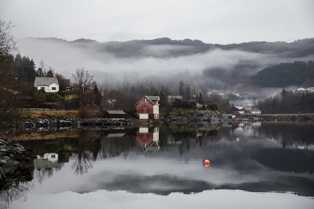 Free photo lake surrounded by buildings with mountains covered in forests and fog reflecting on the water