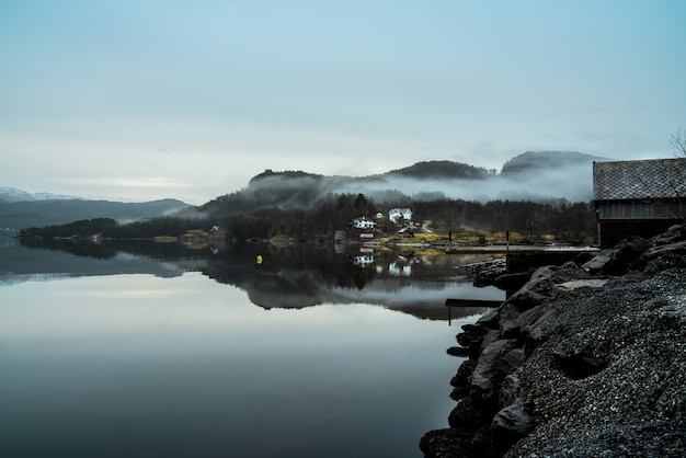 Lake surrounded by hills covered in fog with the greenery reflecting on the water