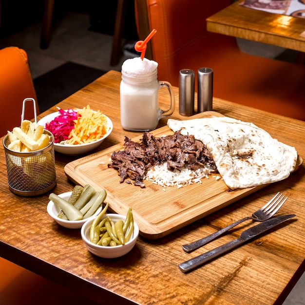 Lamb doner kebab served on top of rice with flatbread pickles ayran and fries