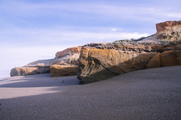 Landscape of the beach surrounded by rocks under the sunlight and a cloudy sky at daytime