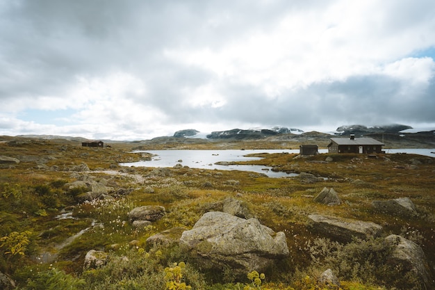 Landscape of a field surrounded by greenery and cabins under a cloudy sky in Finse, Norway