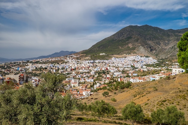 Landscape of hills covered in greenery and buildings under a cloudy sky and sunlight