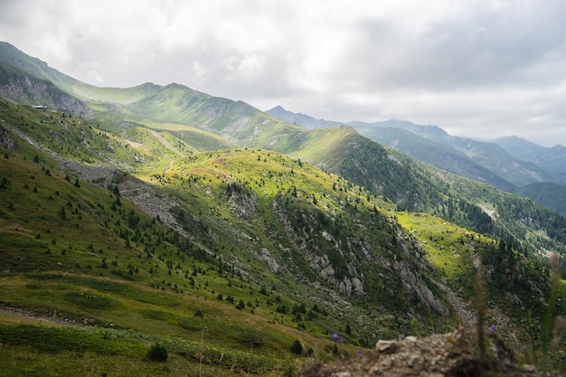 Free photo landscape of hills covered in greenery with rocky mountains under a cloudy sky on the background