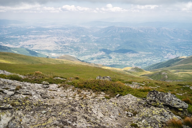 Free photo landscape of hills covered in greenery with rocky mountains under a cloudy sky on the background