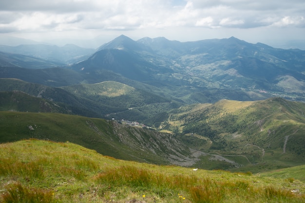 Free photo landscape of hills covered in greenery with rocky mountains under a cloudy sky on the background