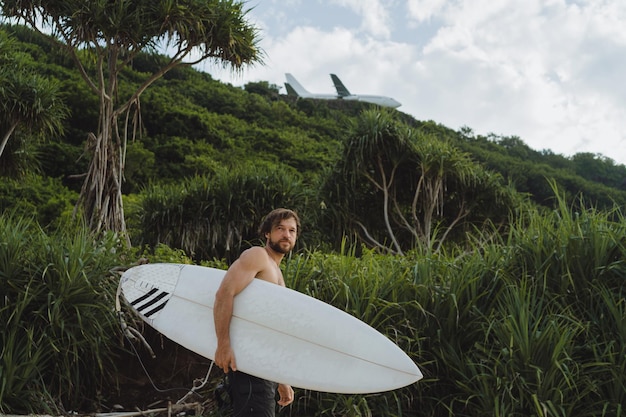 Free photo landscape image of male surfer busy walking on the beach at sunrise while carrying his surfboard under his arm with the ocean waves breaking in the background. young handsome male surfer on the ocean