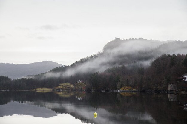 Landscape of a lake surrounded by mountains covered in forests and fog reflecting on the water