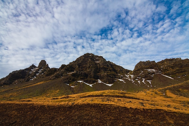 Landscape of rocks covered in greenery and snow under a cloudy sky in Iceland