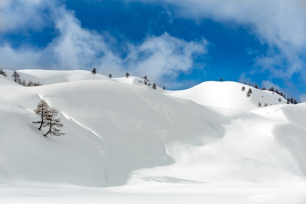 Landscape shot of hills covered with snow in a cloudy blue sky