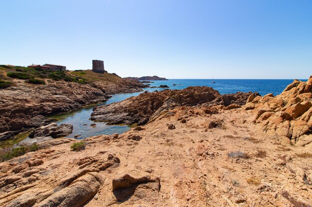 Landscape shot of a seashore with big rocks on the hill in a clear blue sky