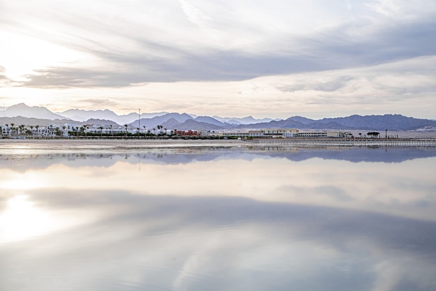 The landscape sky is reflected in the sea. City coastline with mountains on the horizon.