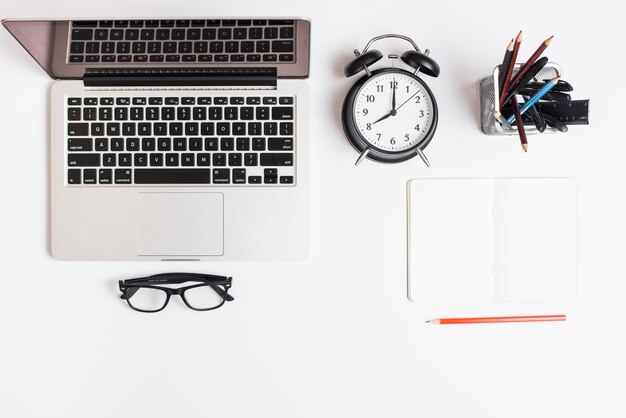 Laptop; alarm clock; eyeglasses; pencil and notepad isolated on white background