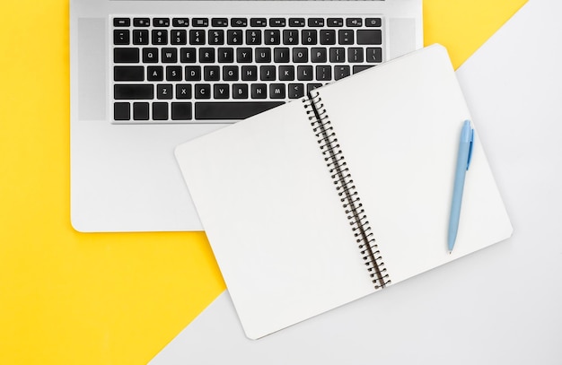 Laptop and blank notepad on color background flat lay workplace concept