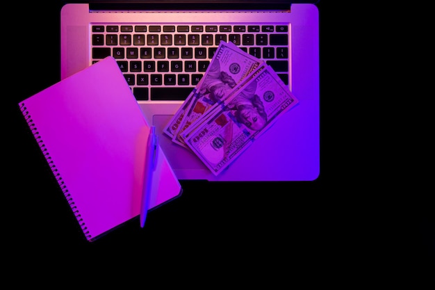 Free photo laptop blank notepad and paper money in neon lighting top view