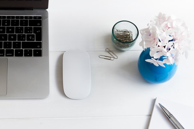 Free Photo laptop and blue vase with pink flowers on desk at workplace