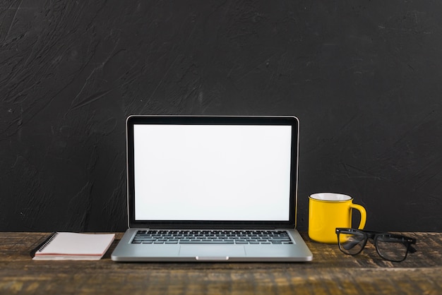 Laptop; cup; notepad and spectacles on wooden surface