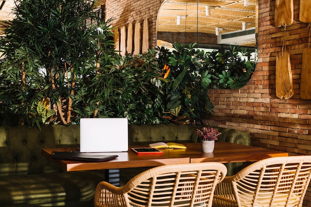 Free photo laptop; digital tablet; book and pot plant on wooden table in the restaurant