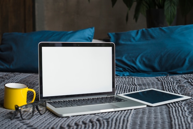 Free photo laptop; digital tablet; spectacles and cup on bed