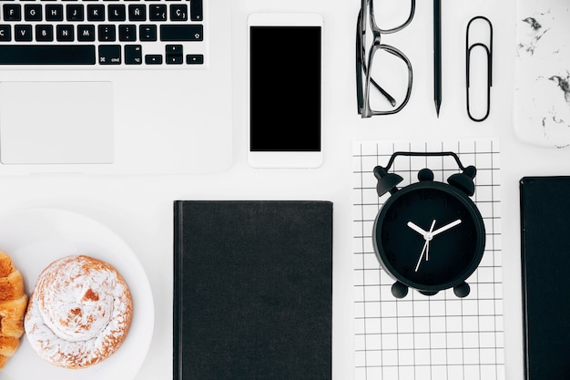 Laptop; mobilephone and digital tablet; eyeglasses; pencil; baked pastry and alarm clock page