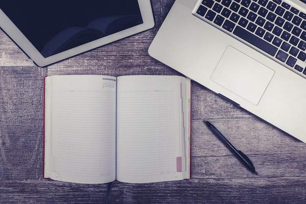 Laptop, open writing notebook and digital tablet from above view on a wooden background