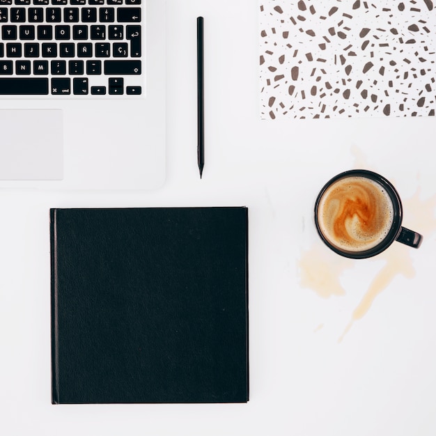 Laptop; pencil; notebook and spilled coffee cup on white background