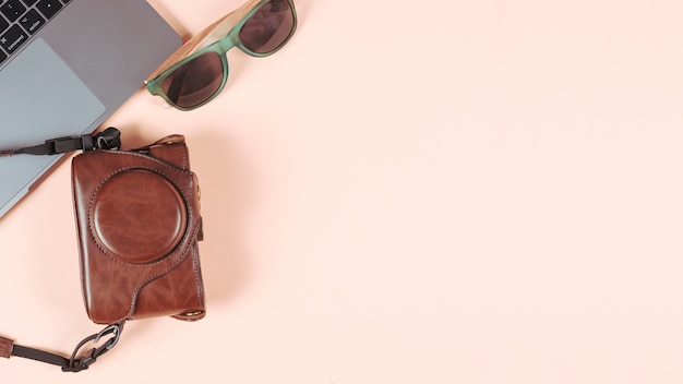 Laptop; sunglasses and camera in its case on plain colored background