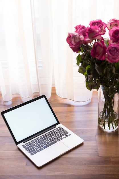 Free Photo laptop next to a vase with flowers