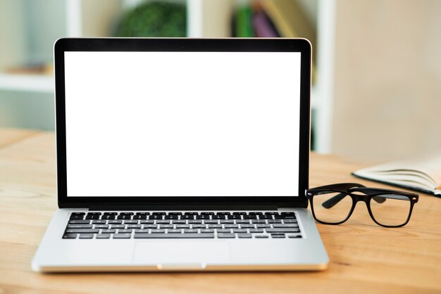 Laptop with blank white screen and eyeglasses on wooden desk