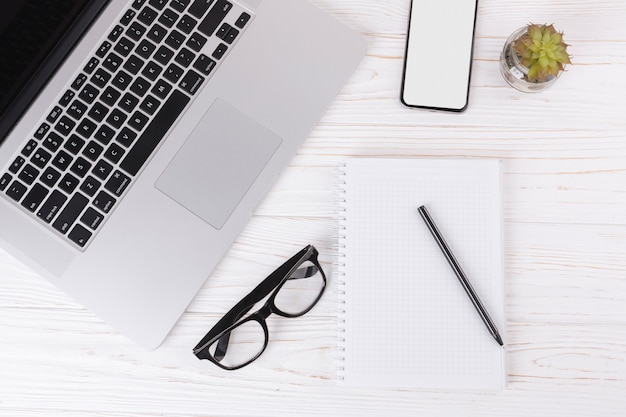 Laptop with notebook and glasses on table