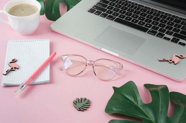 Laptop with notebook and small flamingos on pink table