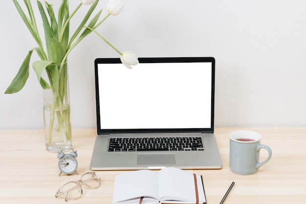 Laptop with white tulips in vase on wooden table