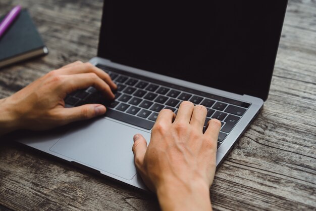 laptop on a wooden table, hands of a man working on a computer