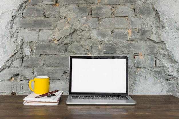 Laptop; yellow cup; and stationeries on wooden table