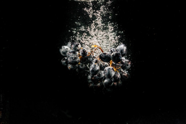 Large bunch of black grape falls on black background